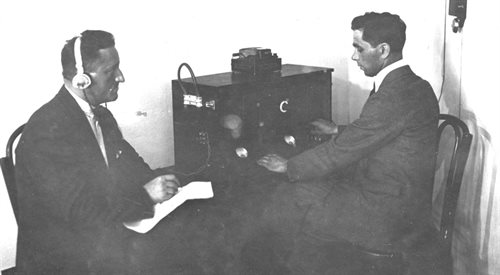 Dwaj mężczyźni siedzą przy pierwszym w Warszawie odbiorniku radiowym