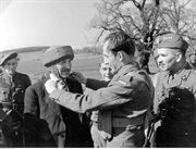 Jeden z żołnierzy zakłada wicepremierowi Wielkiej Brytanii Clementowi Attlee (drugi z lewej) brytyjski ćwiczebny hełm kauczukowy. Na zdjęciu dowódca Brygady, gen. Stanisław Sosabowski (pierwszy z prawej). Ringway w Wielkiej Brytanii, 1944 