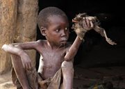 Chłopiec chory na tajemnicy syndrom kiwania, który zabija afrykańskie dzieci siedzi przed swoim domem z martwym kurczakiem w ręku. 