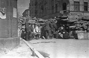 Śródmieście Północne. Grupa powstańców przy barykadzie na ul. Siennej przy skrzyżowaniu z ul. Wielką. Ujęcie w kierunku wschodnim. Po prawej stronie za sanitariuszką stojące butelki zapalające. W tle od prawej widoczne kamienice Sienna 5/7, Sienna 3 i Sienna 1, początek sierpnia 1944.